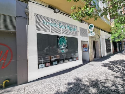 Fachada principal del centro Formación San Miguel en Calle San Juan de la Cruz 30 de Zaragoza, con rotulación corporativa "Formación San Miguel", isotipo grande de la bombilla con árbol del conocimiento en el cristal, y sello RSA Plus de Aragón Empresa pegado al escaparate