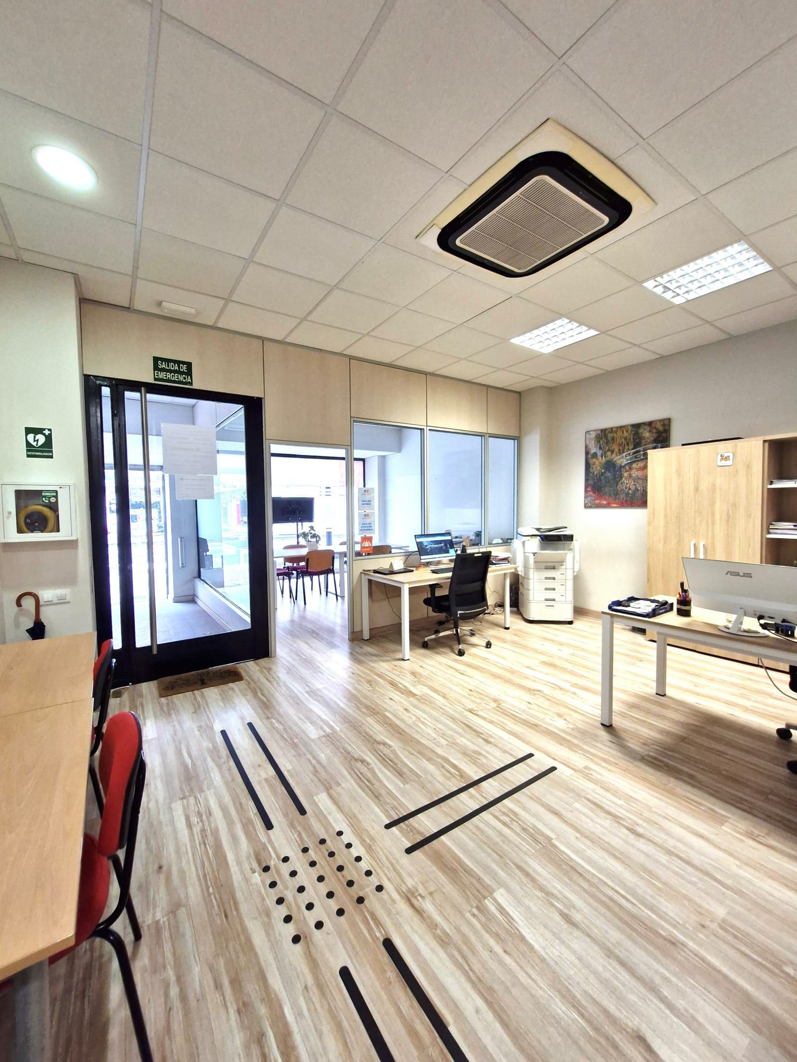 Recepción del centro Formación San Miguel en Zaragoza, con mesa de atención, equipamiento técnico moderno (escáner profesional), vista al exterior con el rótulo Formación San Miguel reflejado en cristal y suelo accesible con guías táctiles